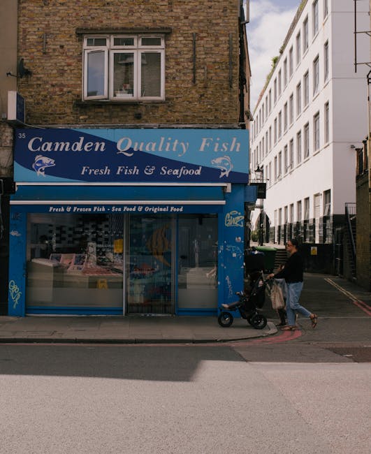 A street scene featuring a two-story brick building with a blue and white sign reading 'Camden Quality Fish' advertising fresh fish and seafood. The building has a large storefront window displaying v